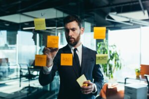 empresario em reflexao em um quadro de tarefas de vidro pendura planos em planos de adesivos de papel colorido para o futuro proximo (1)
